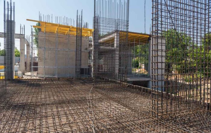 A wide-angle view of a construction site featuring reinforced concrete columns and walls rising behind a vast, intricate grid of steel rebar laid across a structural floor slab.