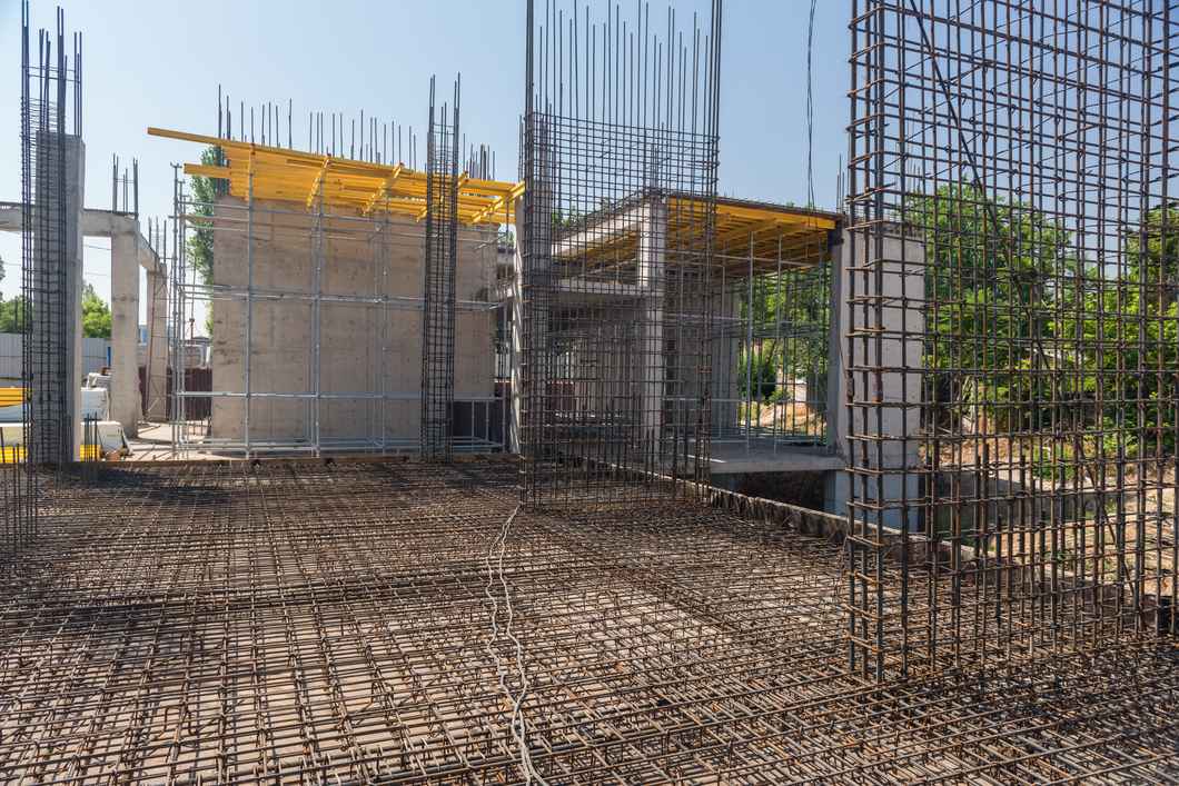 A wide-angle view of a construction site featuring reinforced concrete columns and walls rising behind a vast, intricate grid of steel rebar laid across a structural floor slab.